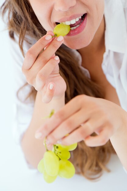 Giovane donna in biancheria intima che mangia l&#39;uva. Isolato su bianco