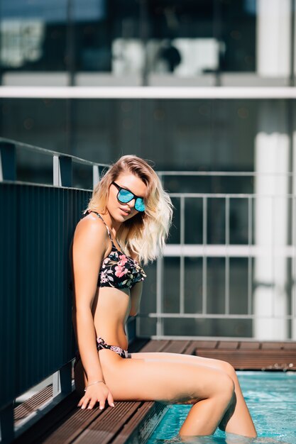 Giovane donna in bikini che si siede sul bordo della piscina