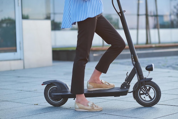 Giovane donna in blaser spogliato sta guidando il suo nuovo scooter elettrico per strada.