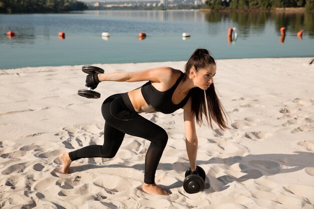 Giovane donna in buona salute che fa squat con i pesi in spiaggia