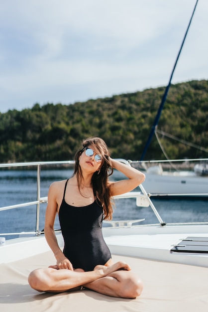 Giovane donna in buona salute e calma che fa yoga sulla barca a vela dell'yacht in mare al fondo dell'isola