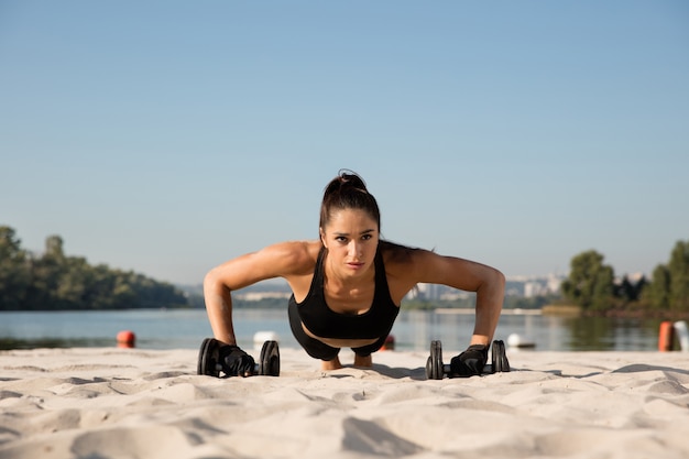 Giovane donna in buona salute formazione parte superiore del corpo con i pesi in spiaggia.