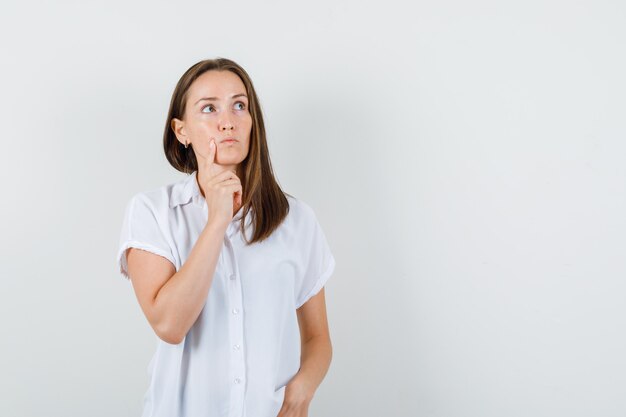 Giovane donna in camicetta bianca che guarda lontano mentre pensa qualcosa e guardando pensieroso