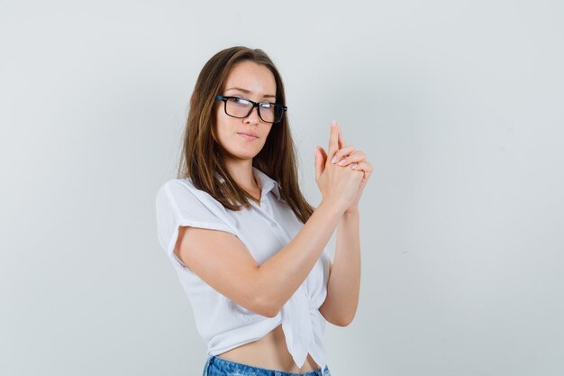 Giovane donna in camicetta bianca che mostra il gesto della pistola e guardando concentrato, vista frontale.