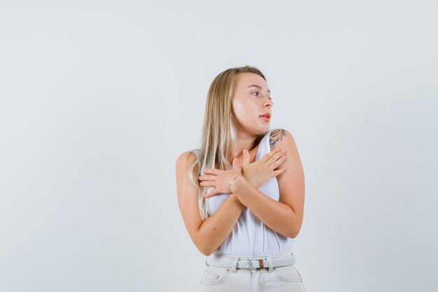 Giovane donna in camicetta bianca che tiene le mani sul petto mentre guarda da parte e sembra ragionevole