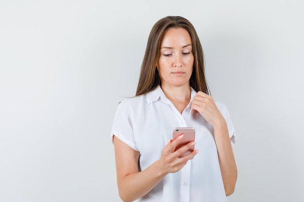 Giovane donna in camicetta bianca guardando il telefono e guardando concentrato