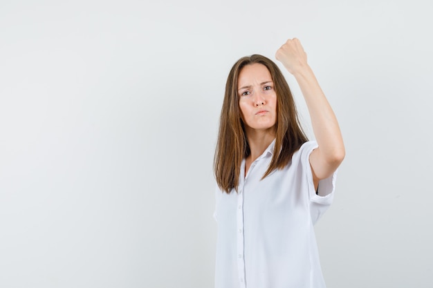 Giovane donna in camicetta bianca, mostrando il suo potere e guardando arrabbiato