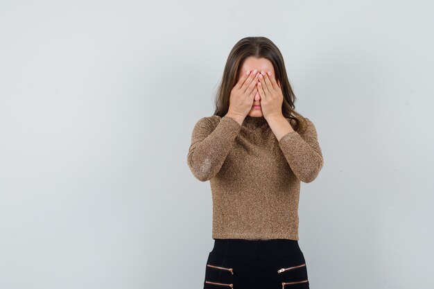 Giovane donna in camicetta dorata che copre gli occhi con le mani