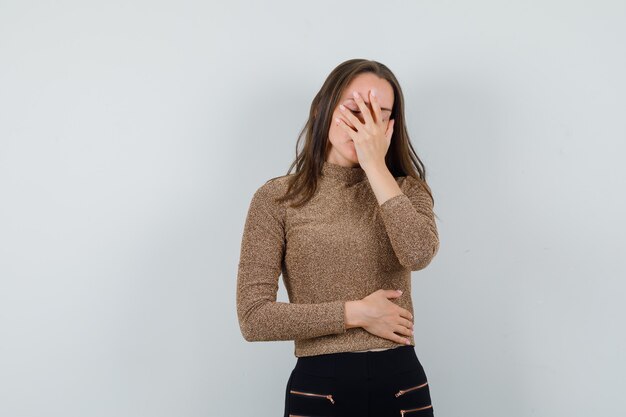 Giovane donna in camicetta dorata tenendo la mano sul viso e guardando annoiato