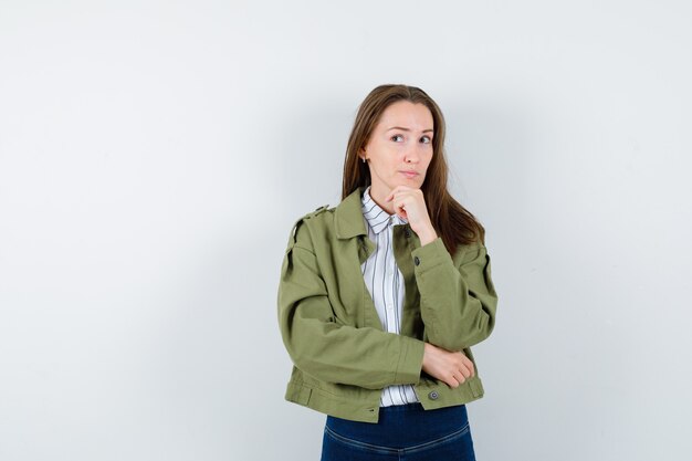 Giovane donna in camicetta, giacca che sostiene il mento a portata di mano e sembra sognante, vista frontale.