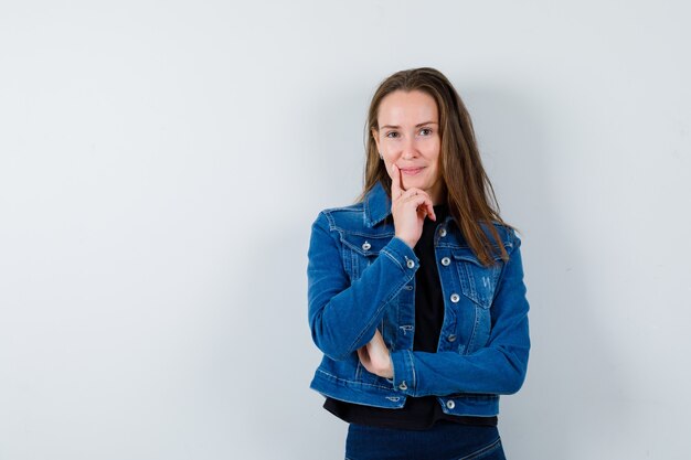 Giovane donna in camicetta, giacca in piedi in posa di pensiero e sguardo fiducioso, vista frontale.