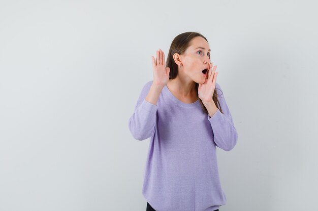 Giovane donna in camicetta lilla chiamando qualcuno ad alta voce e guardando concentrato