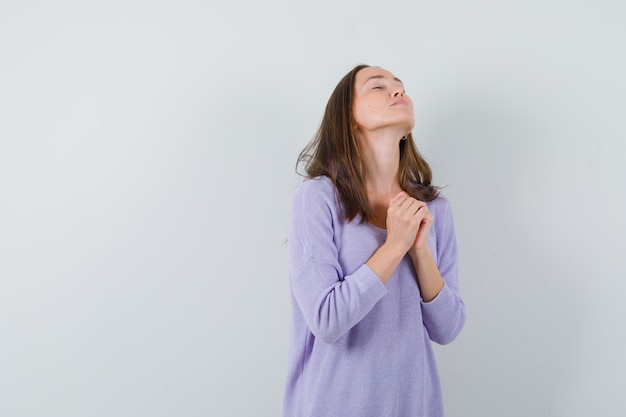 Giovane donna in camicetta lilla pregando e guardando un pio desiderio