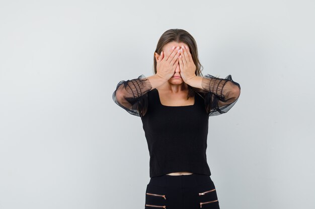 Giovane donna in camicetta nera e pantaloni neri che copre gli occhi con entrambe le mani e sembra stressata