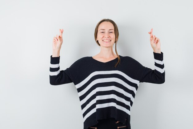 Giovane donna in camicetta nera e pantaloni neri tenendo le dita incrociate e guardando felice