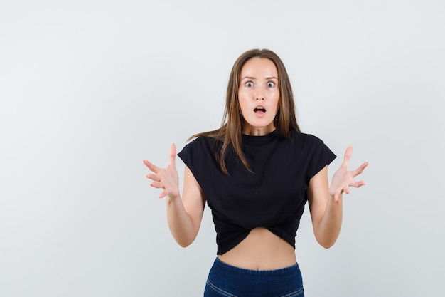 Giovane donna in camicetta nera, pantaloni alzando le mani e guardando eccitato