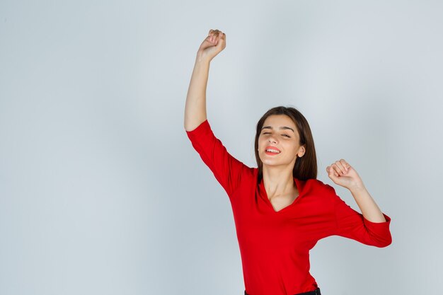 Giovane donna in camicetta rossa, gonna che mostra il gesto del vincitore e sembra beata