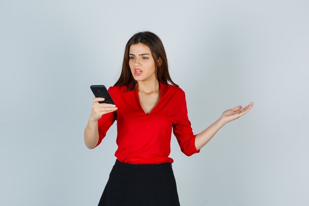Giovane donna in camicetta rossa, gonna guardando il telefono cellulare