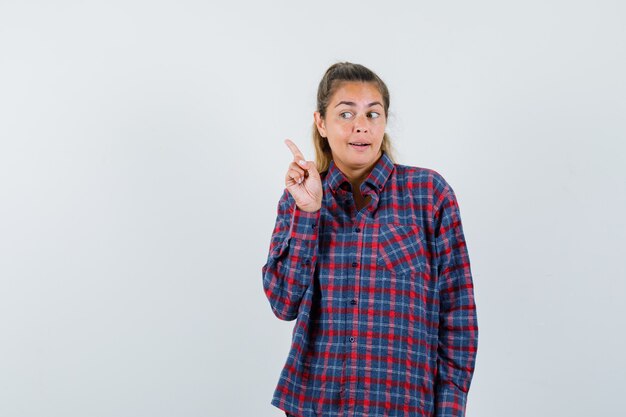 Giovane donna in camicia a quadri alzando il dito indice in gesto di eureka e guardando pensieroso