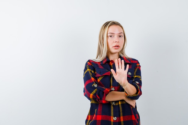 Giovane donna in camicia a quadri che mostra il gesto di arresto e sembra sicura, vista frontale.