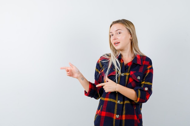 Giovane donna in camicia a quadri che punta al lato sinistro e che sembra felice, vista frontale.