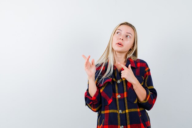 Giovane donna in camicia a quadri che punta all'angolo superiore sinistro e che sembra pensierosa, vista frontale.