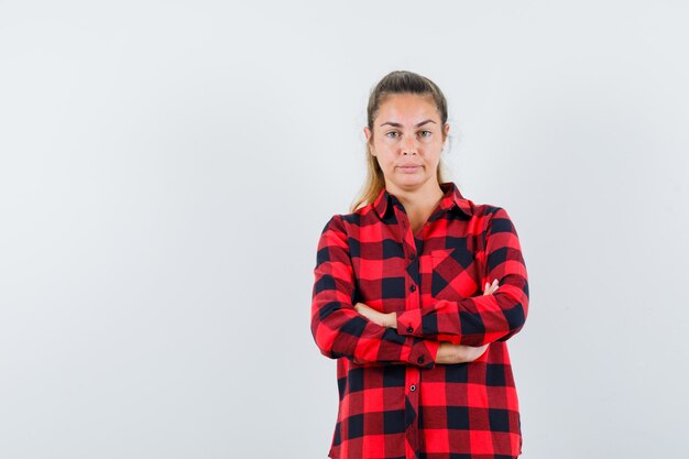 Giovane donna in camicia a quadri in piedi con le braccia incrociate e guardando fiducioso