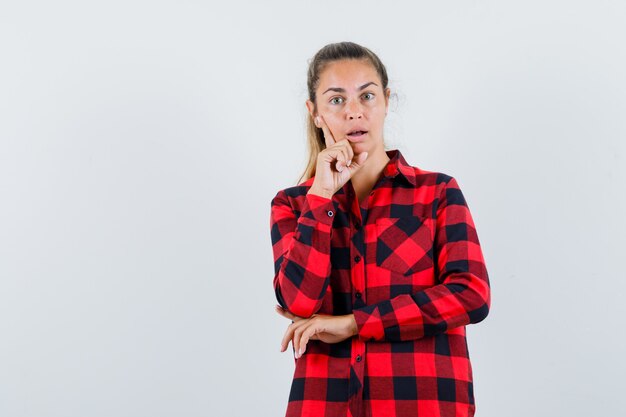 Giovane donna in camicia a quadri in piedi nella posa di pensiero e guardando sorpreso