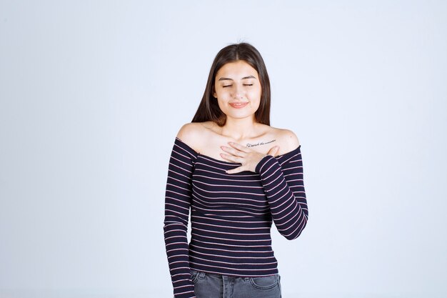 Giovane donna in camicia a righe che indica se stessa con sorpresa