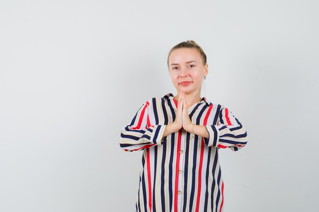 Giovane donna in camicia a righe che mostra il gesto di namaste e sembra allegra