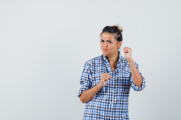 Giovane donna in camicia a scacchi alzando i pugni e guardando aggressivo.