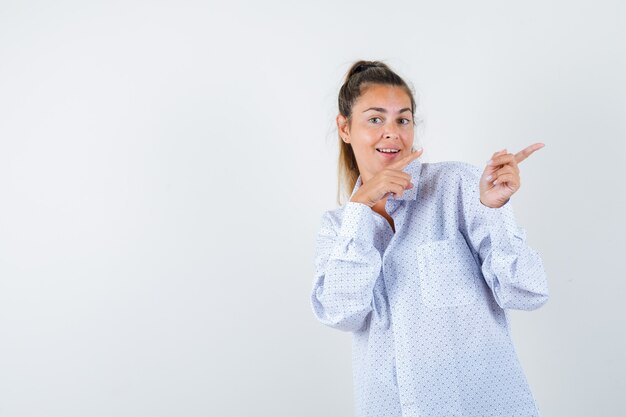 Giovane donna in camicia bianca che punta a destra con il dito indice e che sembra felice