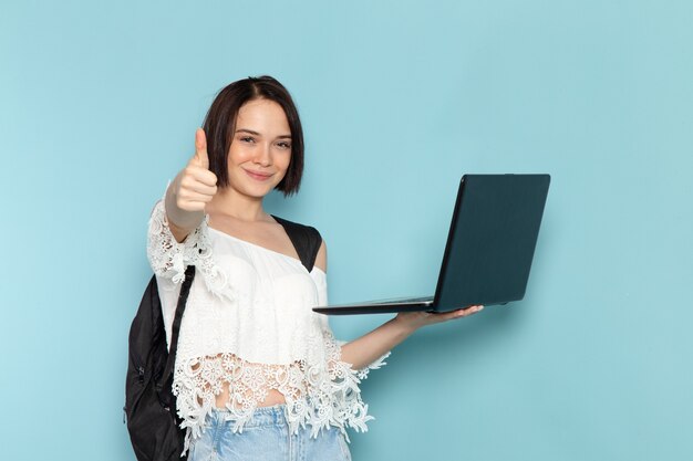 giovane donna in camicia bianca e borsa nera azienda laptop sorridente sul blu