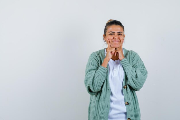 Giovane donna in camicia bianca e cardigan verde menta che mette le dita indice vicino alla bocca e sembra felice