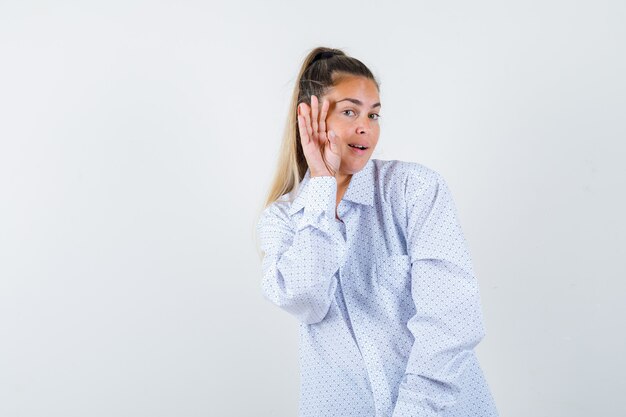 Giovane donna in camicia bianca tenendo le mani vicino al viso come chiamare qualcuno e guardando felice