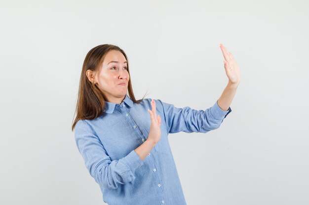 Giovane donna in camicia blu alzando le mani in modo preventivo