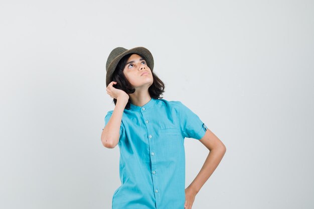 Giovane donna in camicia blu, cappello guardando il cielo