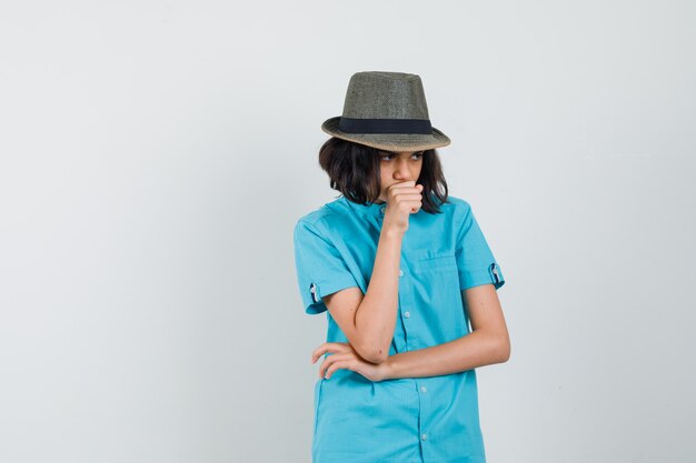 Giovane donna in camicia blu, cappello pensando a qualcosa