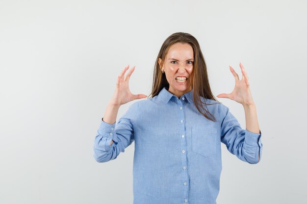 Giovane donna in camicia blu che solleva le mani in modo aggressivo e sembra furiosa