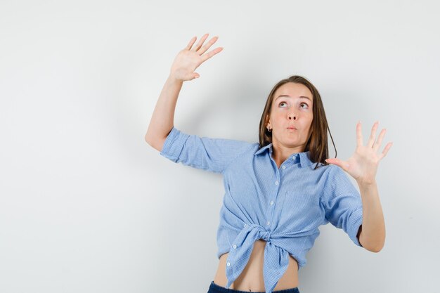 Giovane donna in camicia blu, pantaloni che mostrano il gesto di rifiuto e che sembra spaventata