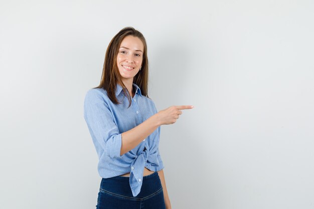 Giovane donna in camicia blu, pantaloni che punta a lato e sembra allegra