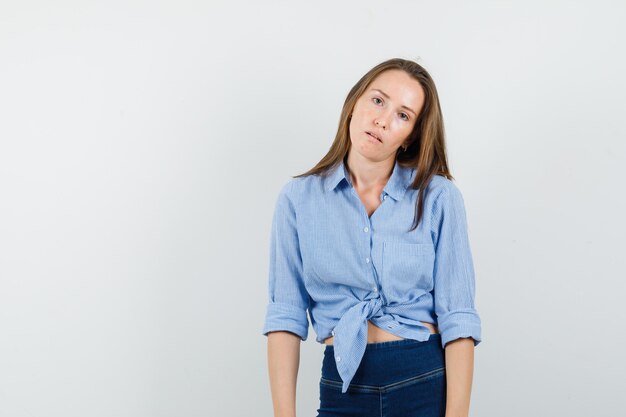 Giovane donna in camicia blu, pantaloni in piedi con la forza e guardando esausto