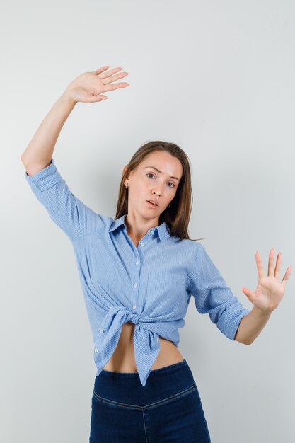 Giovane donna in camicia blu, pantaloni in posa con i palmi sollevati e che sembra carina