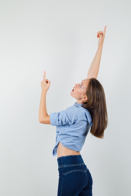 Giovane donna in camicia blu, pantaloni rivolti verso l'alto allungando le braccia e guardando concentrato