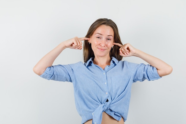 Giovane donna in camicia blu, tappando le orecchie con le dita e guardando preoccupato