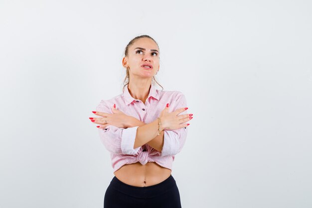 Giovane donna in camicia casual che si abbraccia e che sembra pensierosa, vista frontale.