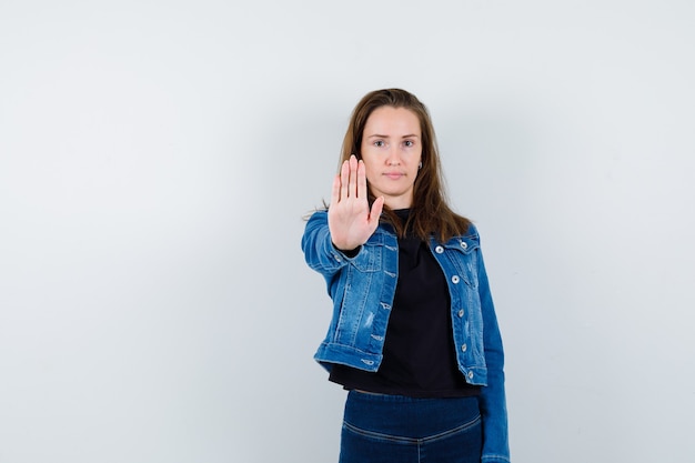 Giovane donna in camicia che mostra il gesto di arresto e sembra sicura, vista frontale.