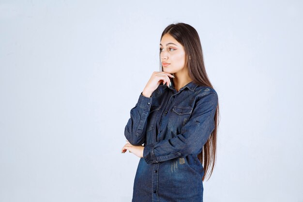 Giovane donna in camicia di jeans che dà pose neutre e seducenti senza reazioni