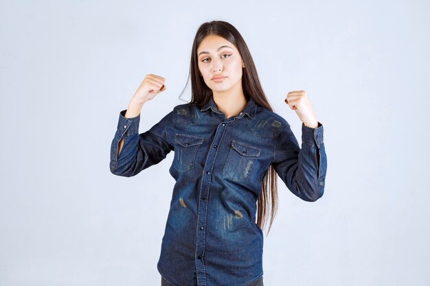 Giovane donna in camicia di jeans che mostra i suoi muscoli del braccio