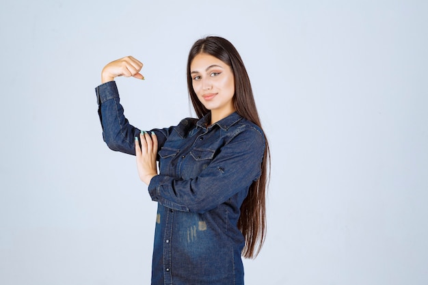 Giovane donna in camicia di jeans che mostra i suoi muscoli del braccio